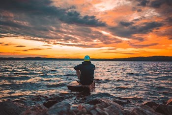 man sitting on gray rock during sunset