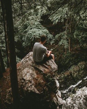 man sitting on gray rock near the cliff at daytime