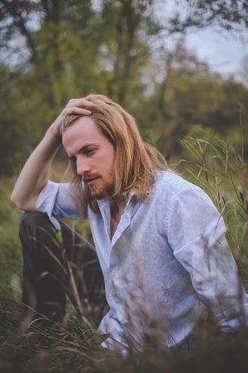 man sitting on green grass touching hair during daytime