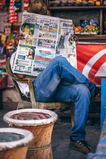 Man Sitting on Plastic Armchair Reading Newspaper