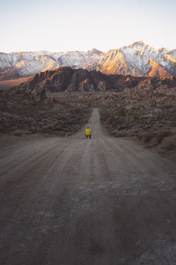 man sitting on road between rock mountains at daytime