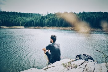 Man Sitting On Rock Cliff Looking At Body Of Water