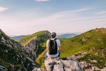 Man Sitting on Rock Facing the Grass Covered Mountains
