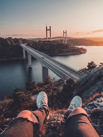 Man Sitting on Rock Near Bridge