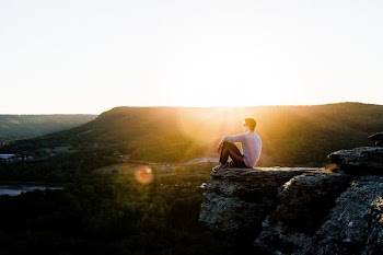 man sitting on rock near cliff with overlooking mountains