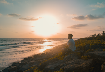 Man Sitting on Rocks Near Body of Water
