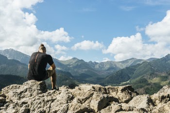 Man Sitting on Rocks Within Mountain Range