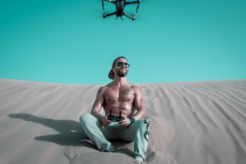 Man Sitting on Sand Controlling Drone