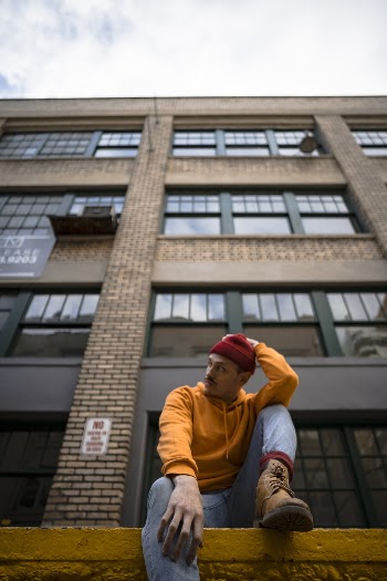 Man Sitting on Sidewalk in Front of Brick Building