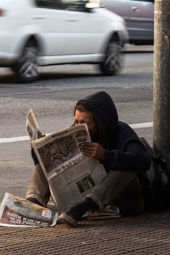 Man Sitting on sidewalk Reading Newspaper