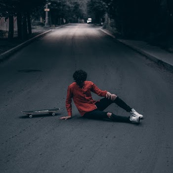 Man Sitting on Street next to Skateboard