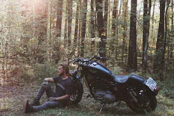 Man Sitting on the Ground Leaning Back on Parked Motorcycle 