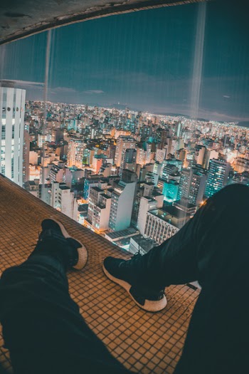 Man Sitting on Top of Building Near Glass Window Viewing Cityscape