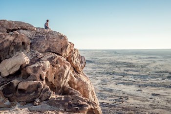 man sitting on top of rock formation near beach