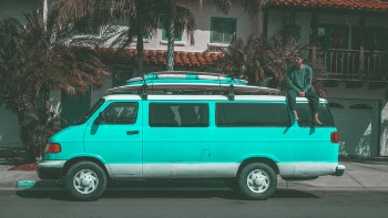 Man Sitting on Top of Teal Dodge Ram Van Parked Near House