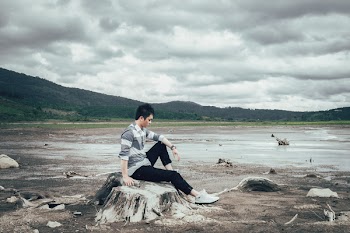 Man Sitting on Tree Stump Near Body of Water