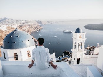 man sitting on white concrete wall facing large body of water during daytime