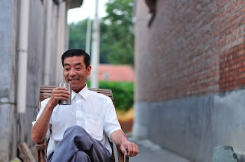 Man Sitting on Wooden Chair Holding a Glass of Drink