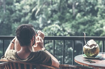 Man Sitting on Wooden Chair With Foot on Black Steel Railings