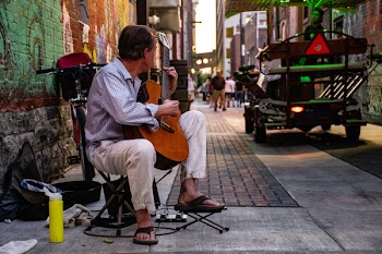 Man Sitting Playing Classical Guitar on Gray Road