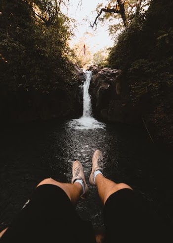man sitting while facing waterfalls during daytime