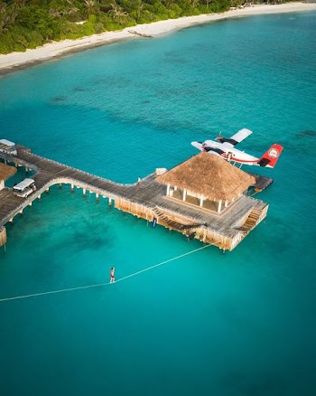 Man slacklines across his resort villa in the Maldives next to a sea plane