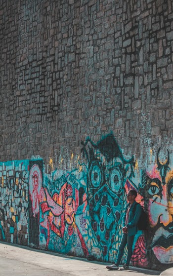 Man Standing and Leaning on Wall With Graffiti Painting