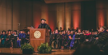 Man Standing at a Center of Stages on Podium Surrounded by People