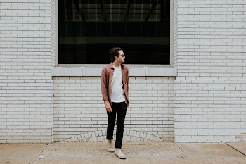 man standing beside beige brick wall