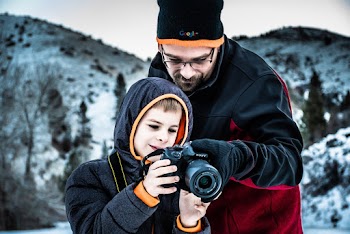 Man Standing Beside Boy While Holding Dslr Camera in Selective Focus Photography