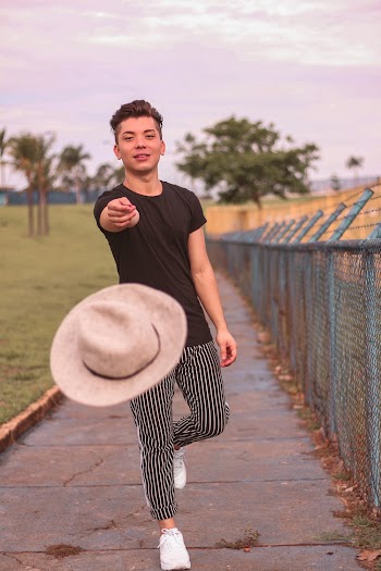 Man Standing Beside Fence Throwing a Hat