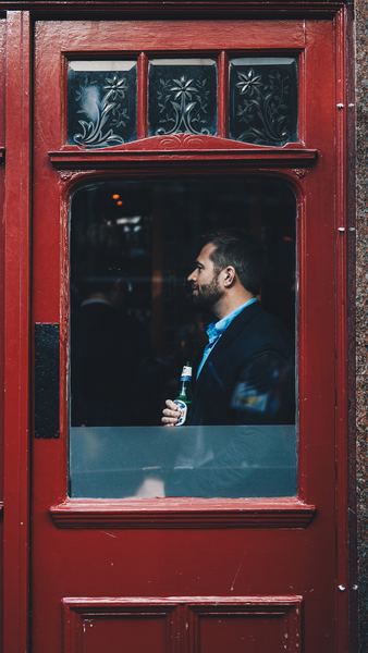 man standing beside red wooden glass door inside the building
