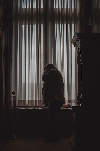 Man Standing Beside Window With Curtain