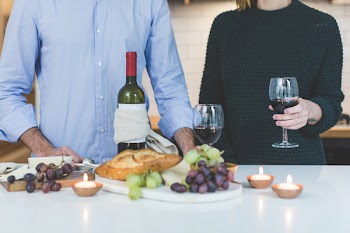 Man Standing Beside Woman Holding Wine Glass in Front of Grapes and Bread on Table
