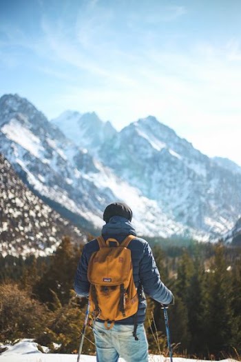 man standing holding snow stick facing mountain