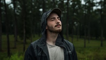 man standing in between green trees closing his eyes during daytime