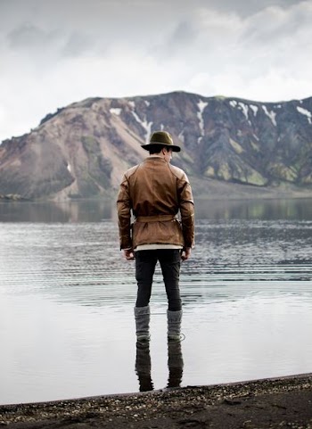 man standing in body of water facing toward mountain
