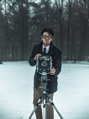 man standing in front of black camera with stand surrounded by trees