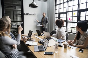 Man Standing in Front of Board With People Sitting Inside a Room