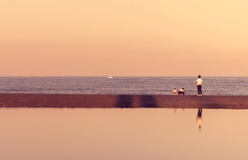 Man Standing Near Seashore With Boat in Distance Under Cloudy Sky during Daytime