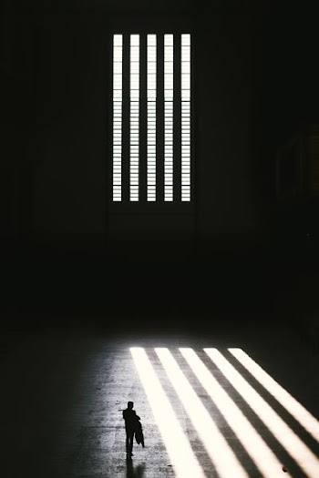 man standing near window with window blinds grayscale photography