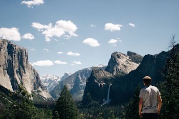man standing next to mountains with waterfalls and trees