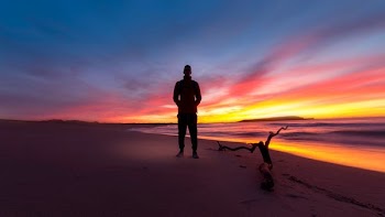 man standing on a beach during sunset