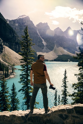 Man Standing on a Stonewall looking at the Mountains and Body of Water