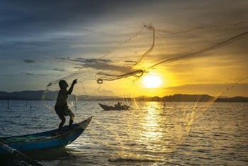 Man Standing On Boat Throwing Net