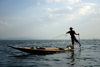 Man Standing on Brown Boat on Body of Water Under White and Blue Sky