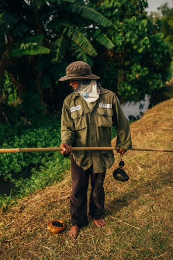 Man Standing on Brown Grass Holding Brown Bamboo Pole