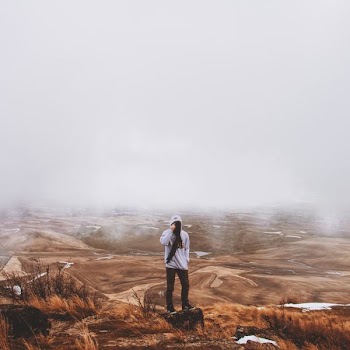 man standing on brown hill surrounded with mist