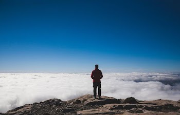 man standing on brown mountains facing sea of clouds