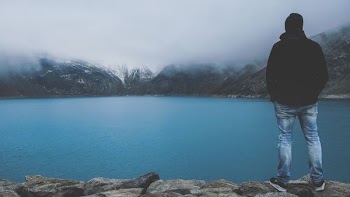 man standing on cliff facing bod of water